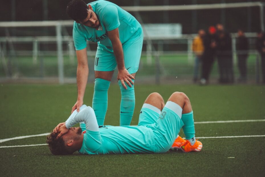 Soccer player lying on the field being checked on by a teammate after a sports injury, illustrating summer sports injuries in Markham